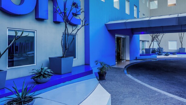 Un edificio moderno con un llamativo letrero 'One', plantas en macetas y una entrada curva.
