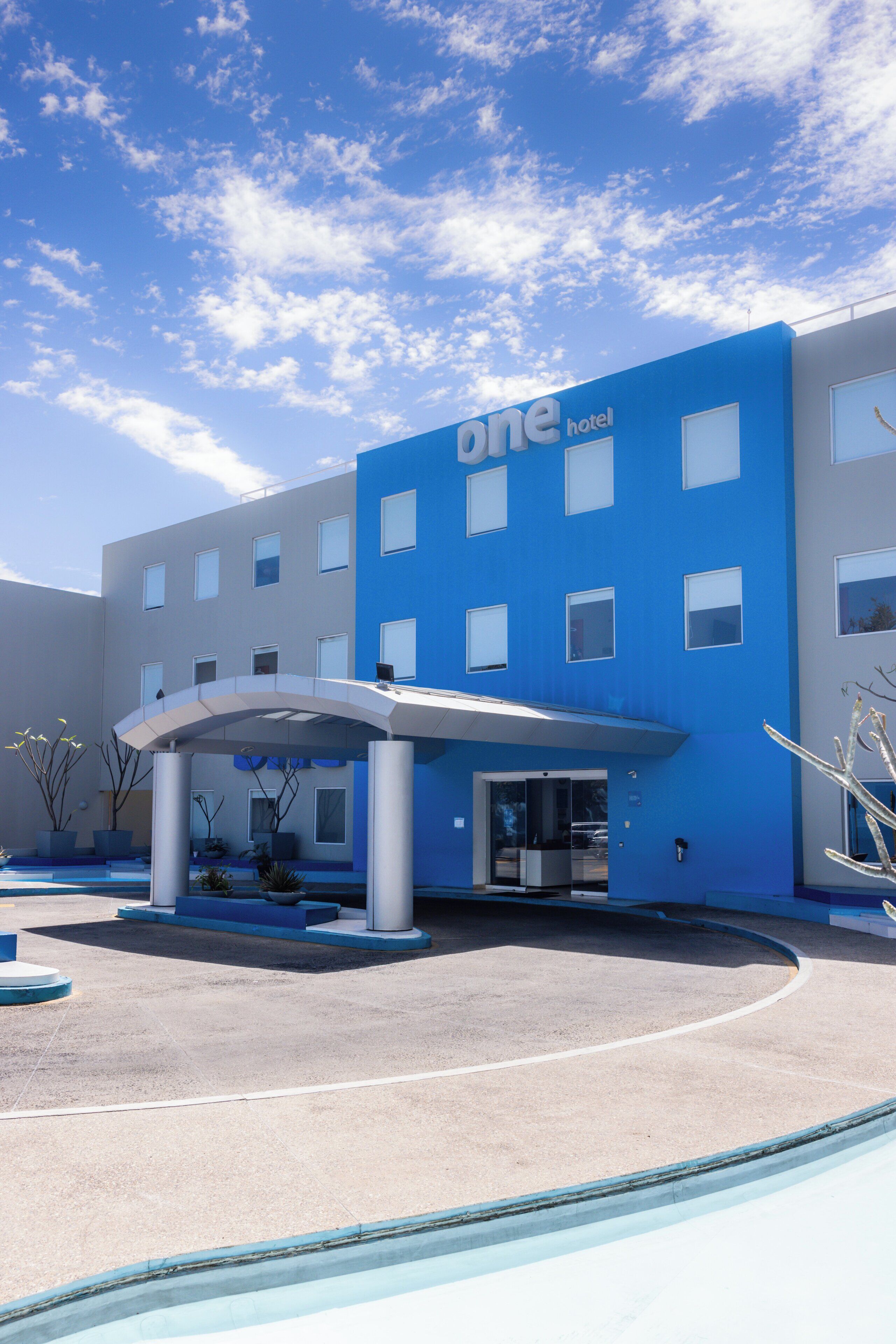 Un hotel moderno con fachada azul, acceso cubierto y zona de piscina.