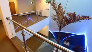 Un moderno vestíbulo de hotel con barandilla de cristal, una planta decorativa y un elemento mural iluminado en azul.