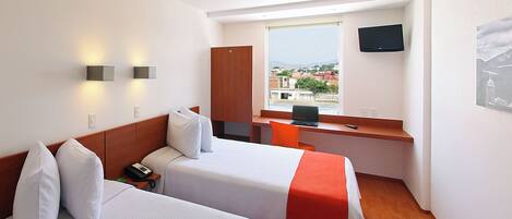 A hotel room with two beds, a desk, a chair, a TV, and a window with a city view.