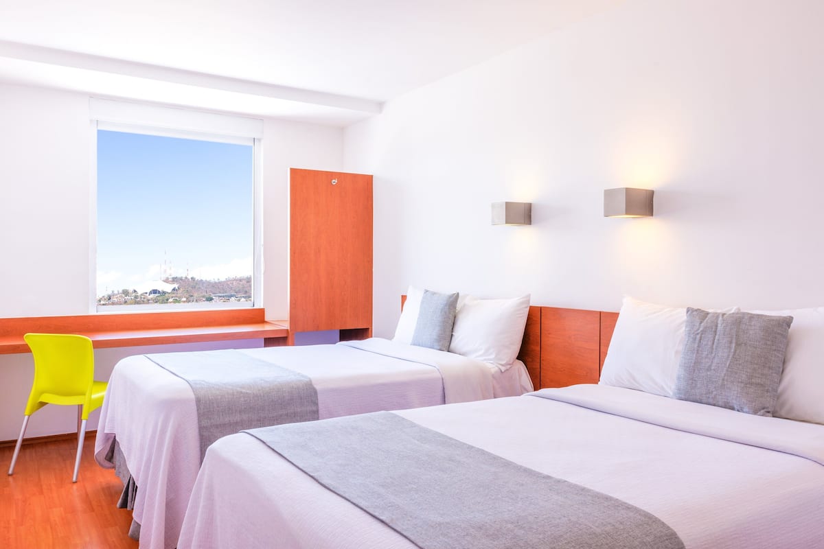 A hotel room with two beds, a desk, a chair, and a large window with a view.