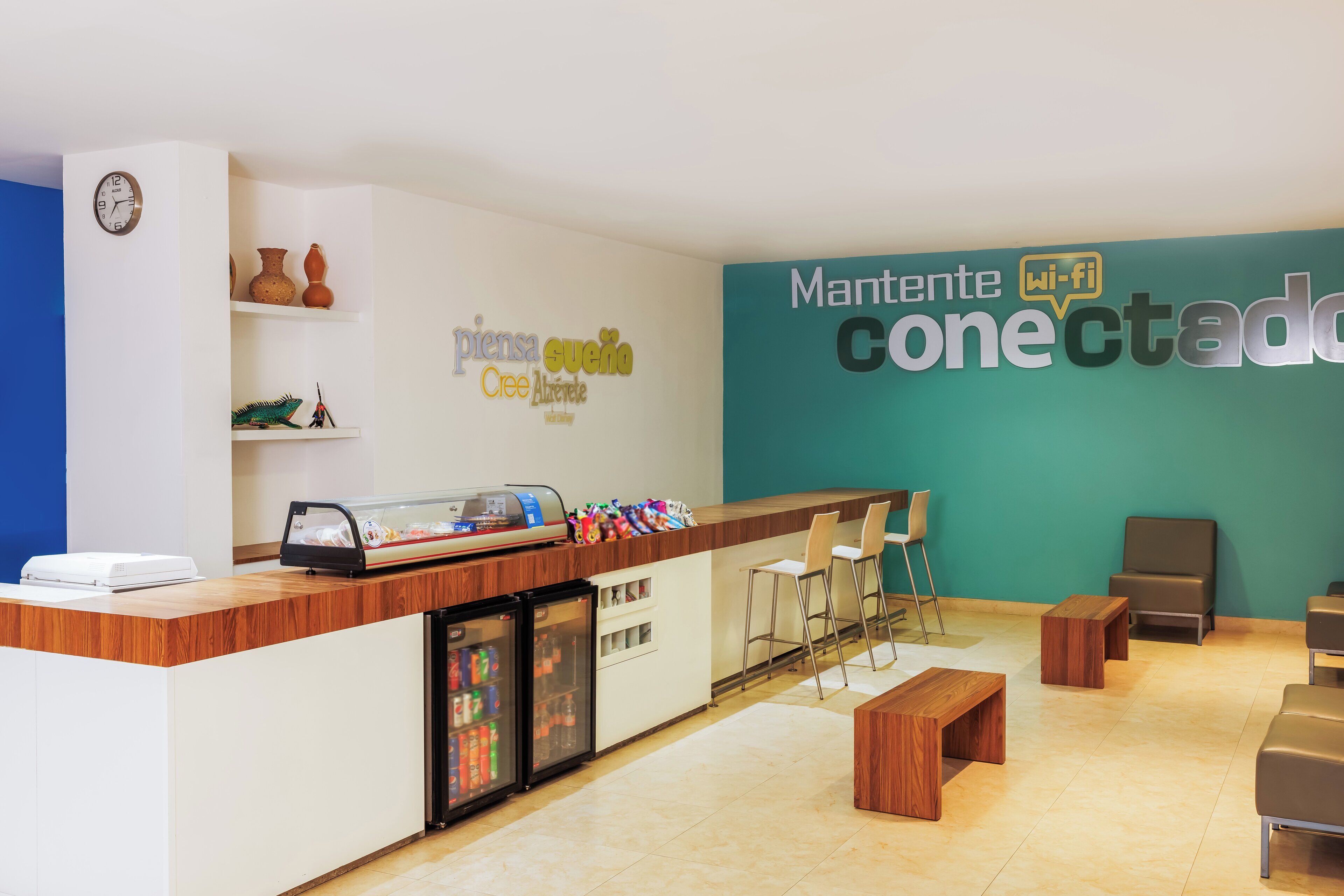 Zona de recepción con mostrador de madera, un reloj, un refrigerador y asientos.
