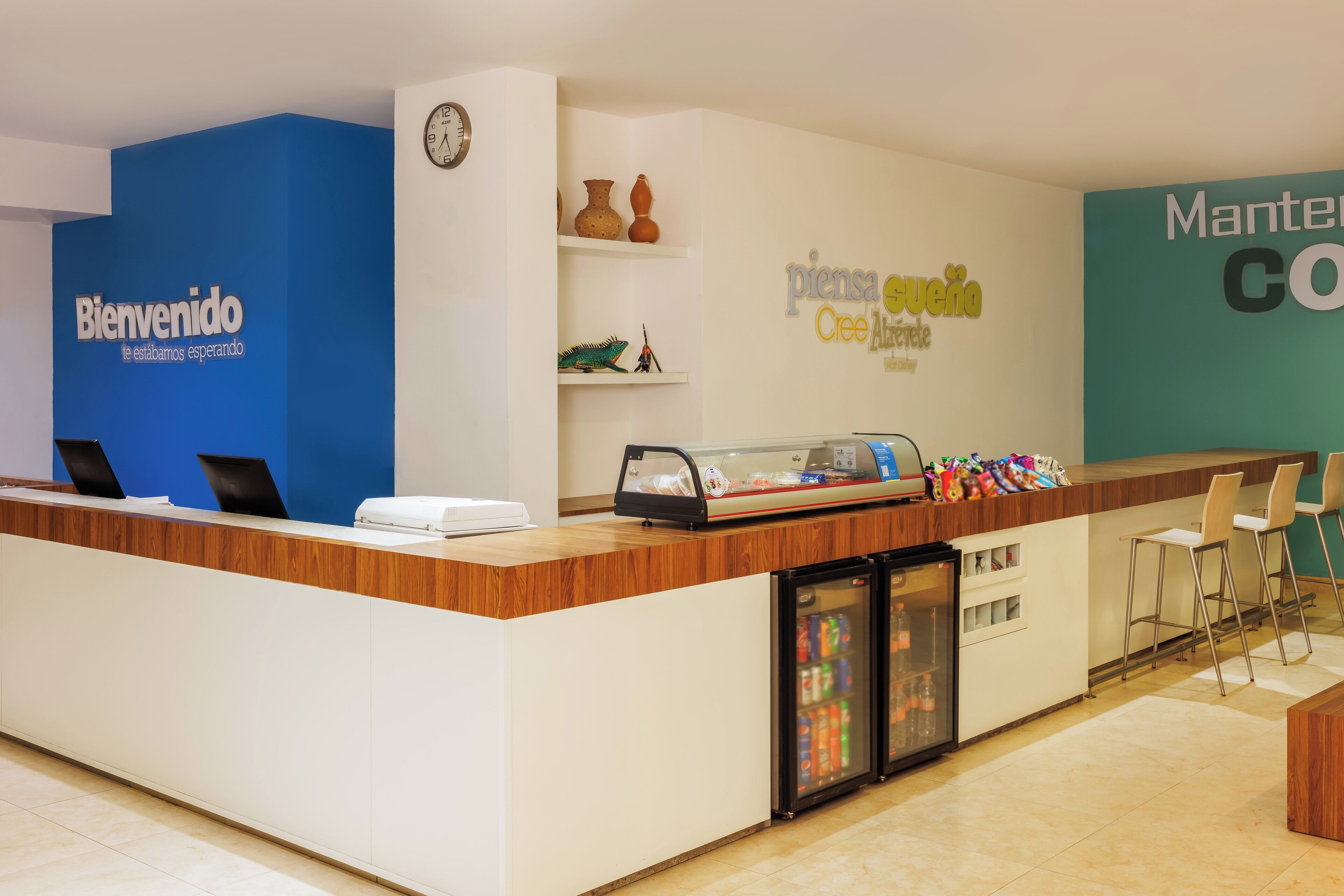 Un mostrador de recepción con pared azul, un reloj y un letrero en la pared que dice "Bienvenido estamos esperando".