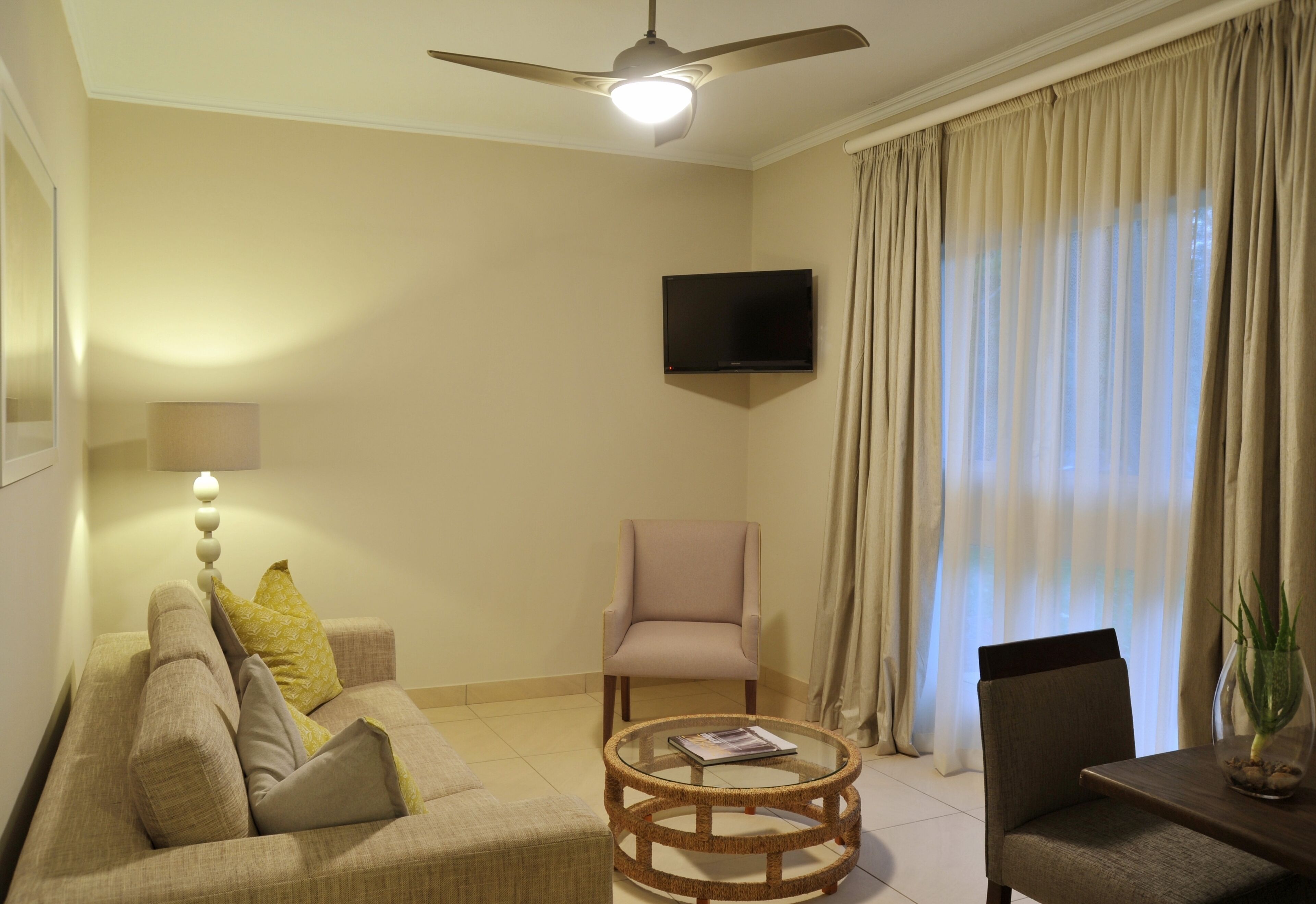 Uma sala de estar com sofá, poltronas, mesa de centro, televisão e ventilador de teto.