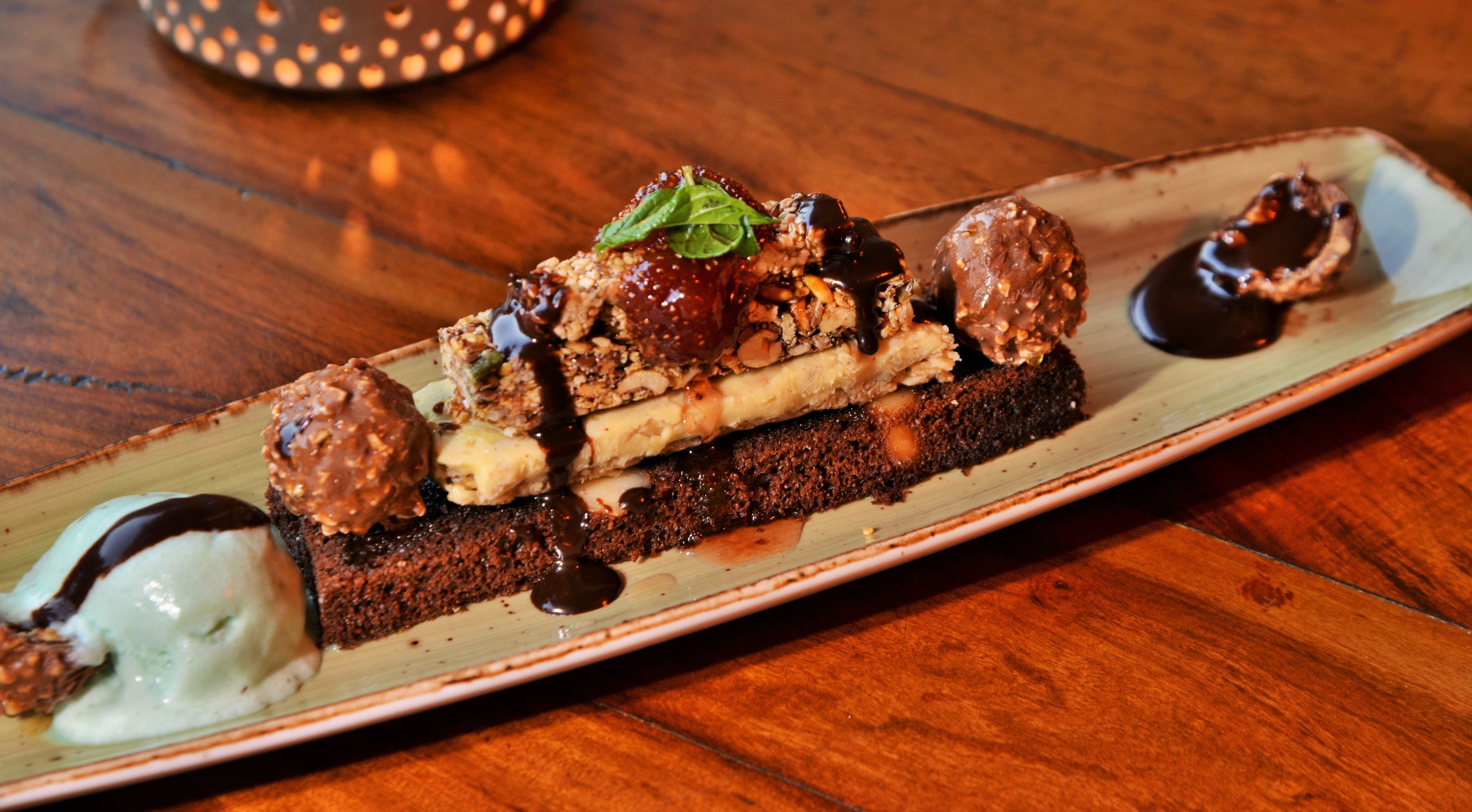 A dessert plate with various sweets and a chocolate-covered item on a wooden table.
