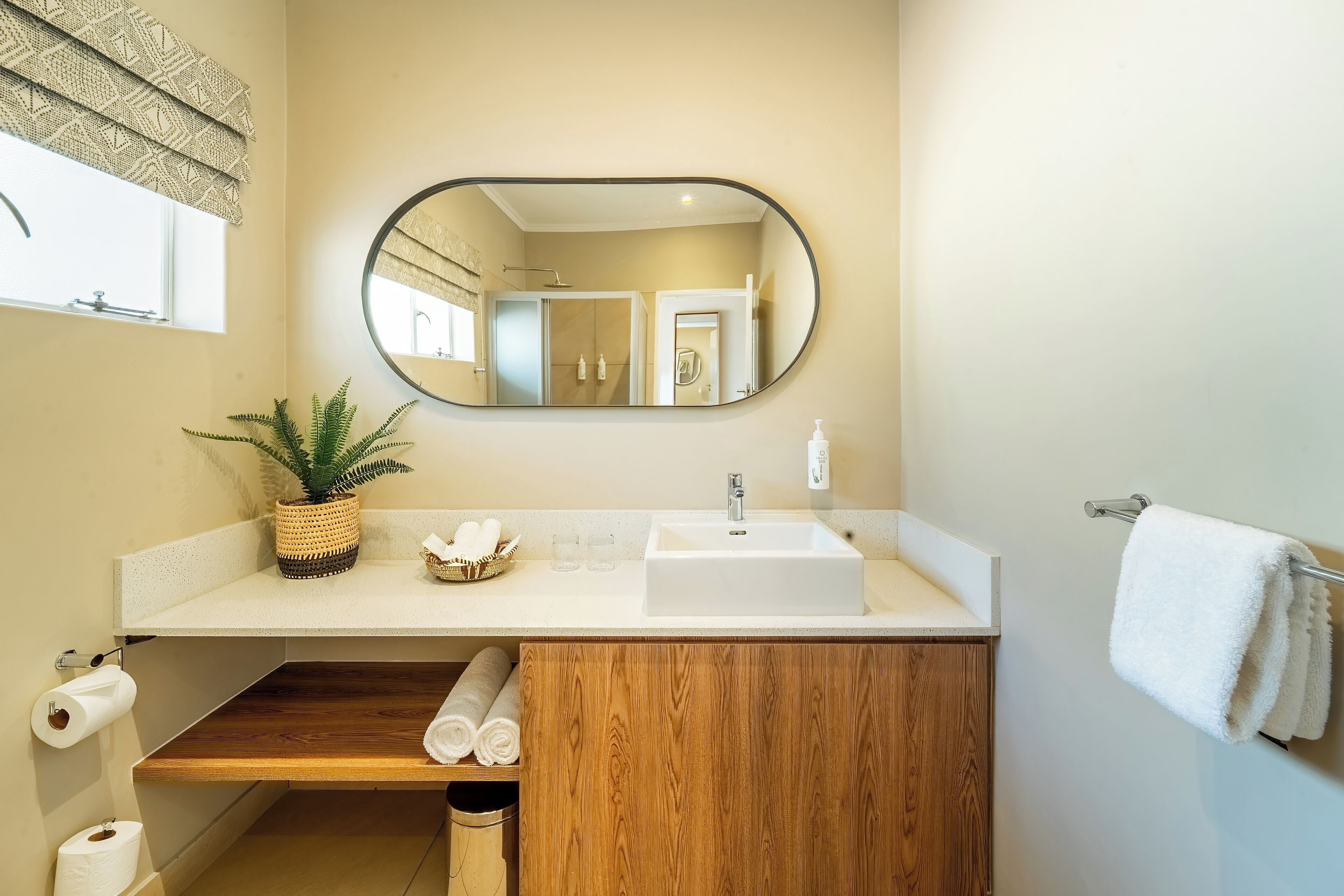 A bathroom with a wooden vanity, a sink, a mirror, a towel rack, and a potted plant.