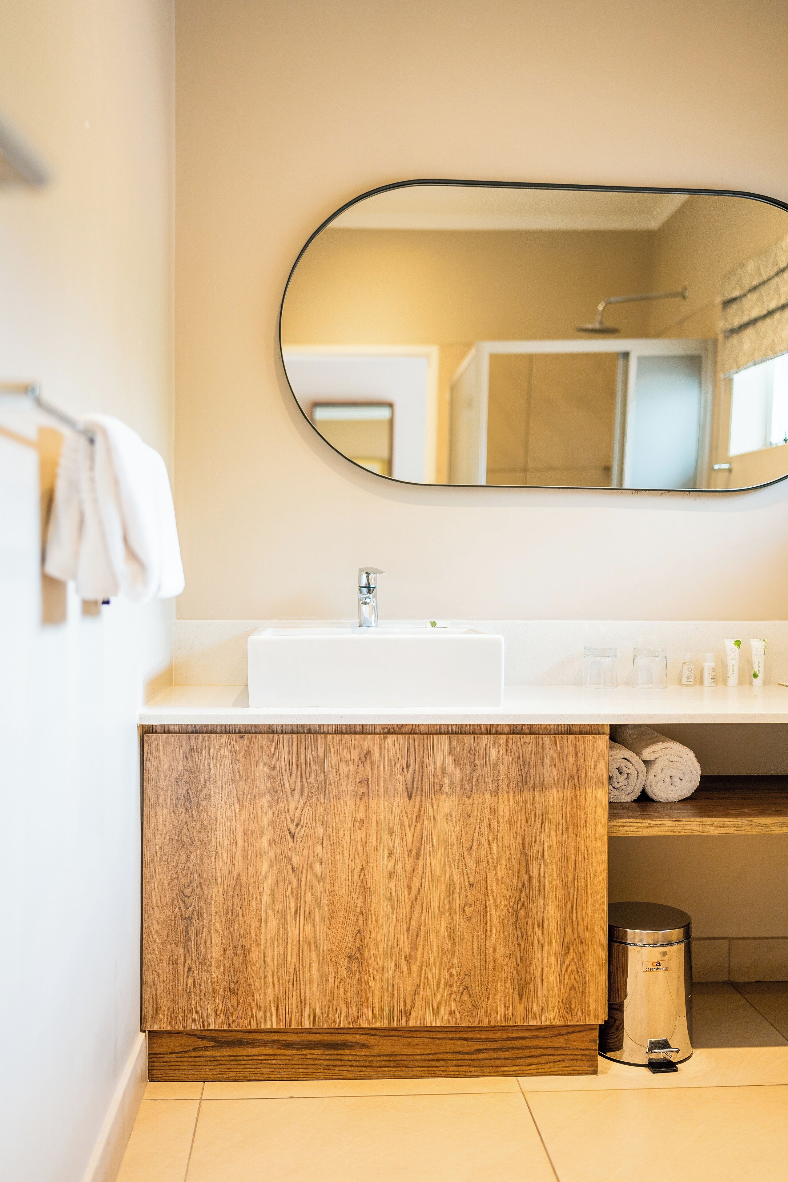 Une salle de bain moderne avec un meuble-lavabo en bois, un lavabo blanc et un miroir rond.