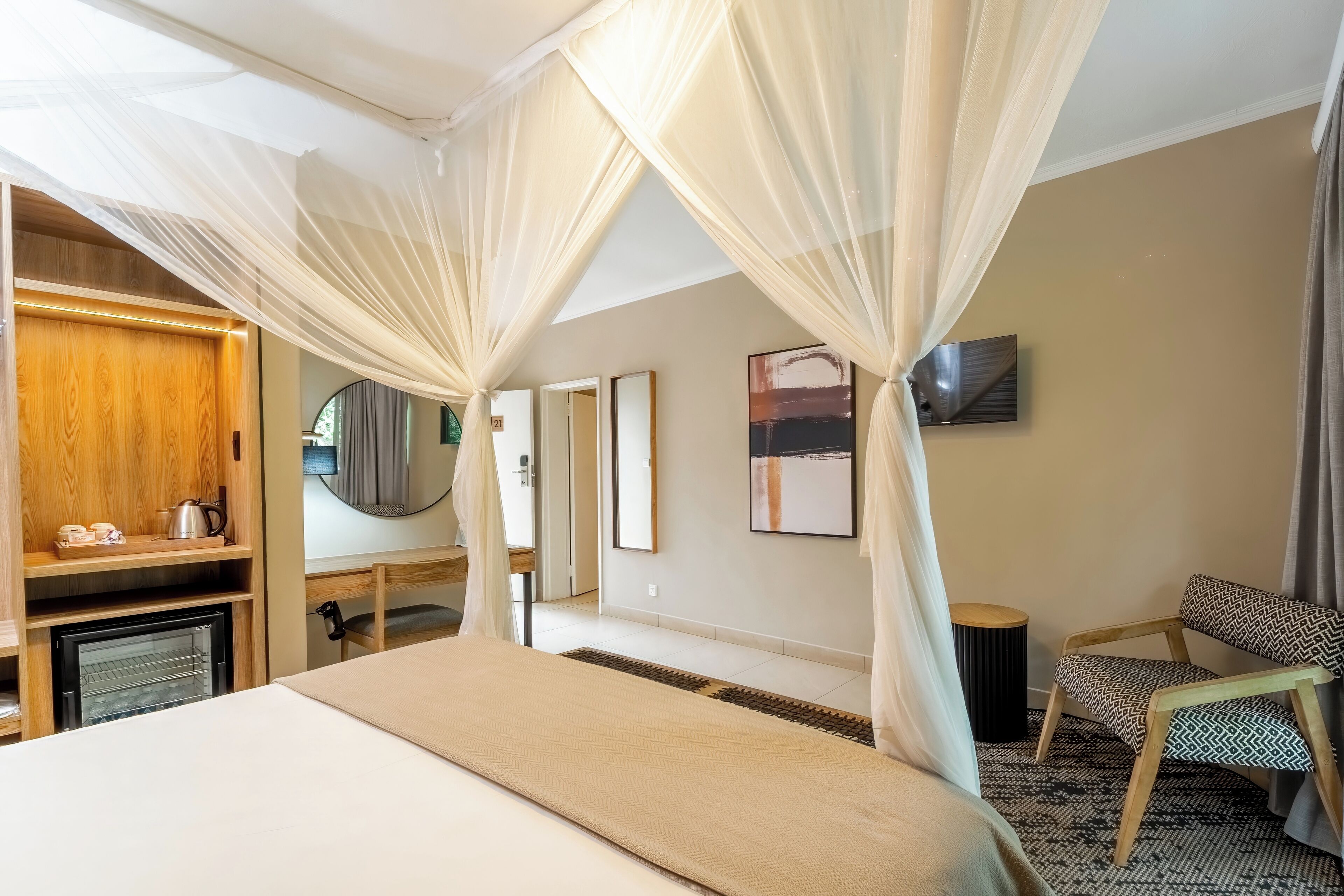 A hotel room with a bed, a wooden wardrobe, a mirror, a television, and a chair.