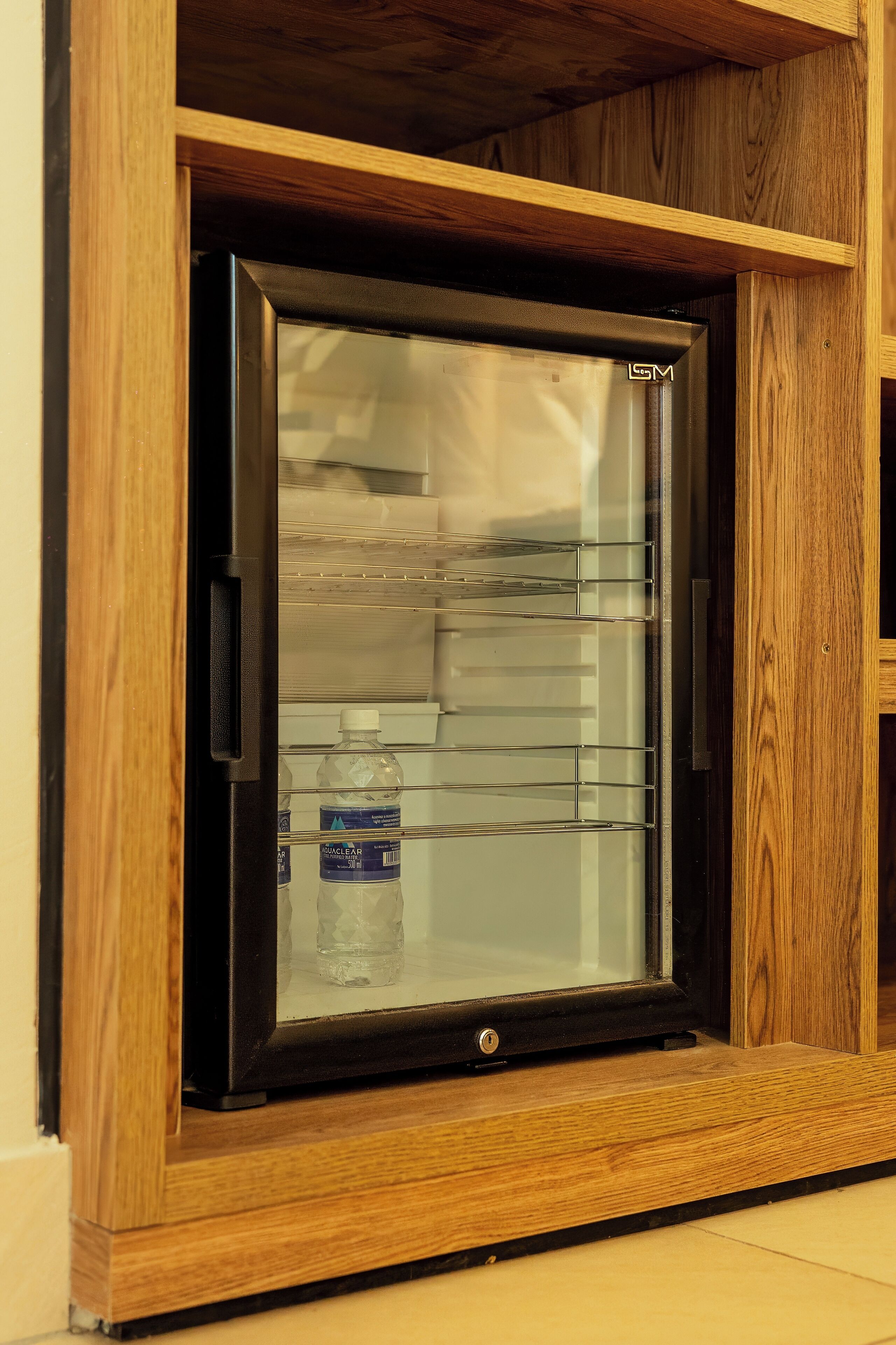 A compact refrigerator with a wooden frame, a water dispenser, and a single bottle of water inside.
