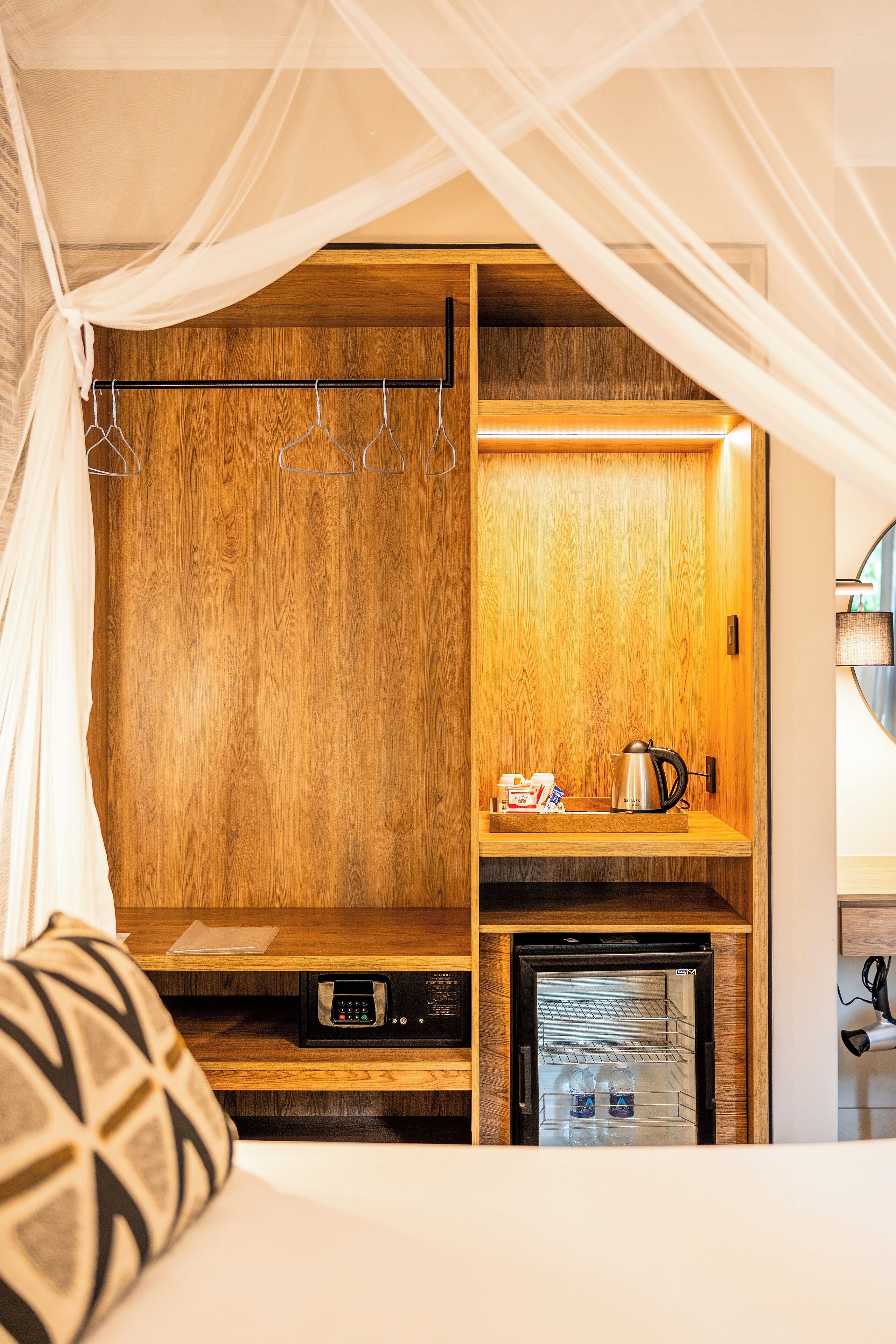 Un dormitorio con cama a dosel, un armario de madera, una pequeña kitchenette y una mesita de noche con hervidor y tazas.
