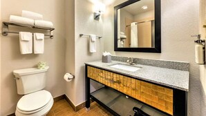 Ein modernes Badezimmer mit Toilette, Waschbecken und Spiegel. Handtücher befinden sich an einem Wäscheständer und ein Taschentuchhalter steht auf dem Waschbecken.