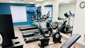 Ein Fitnessraum mit Laufbändern, Crosstrainern und einer Bank.