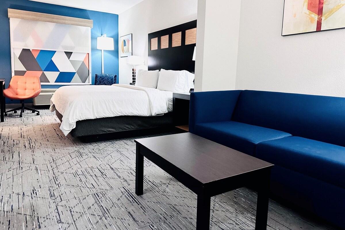 A hotel room with a bed, a blue sofa, a small table, and a chair.