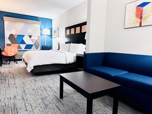 Una habitación de hotel con una cama, un sofá azul, una mesita, una silla y una pared con un estampado geométrico.