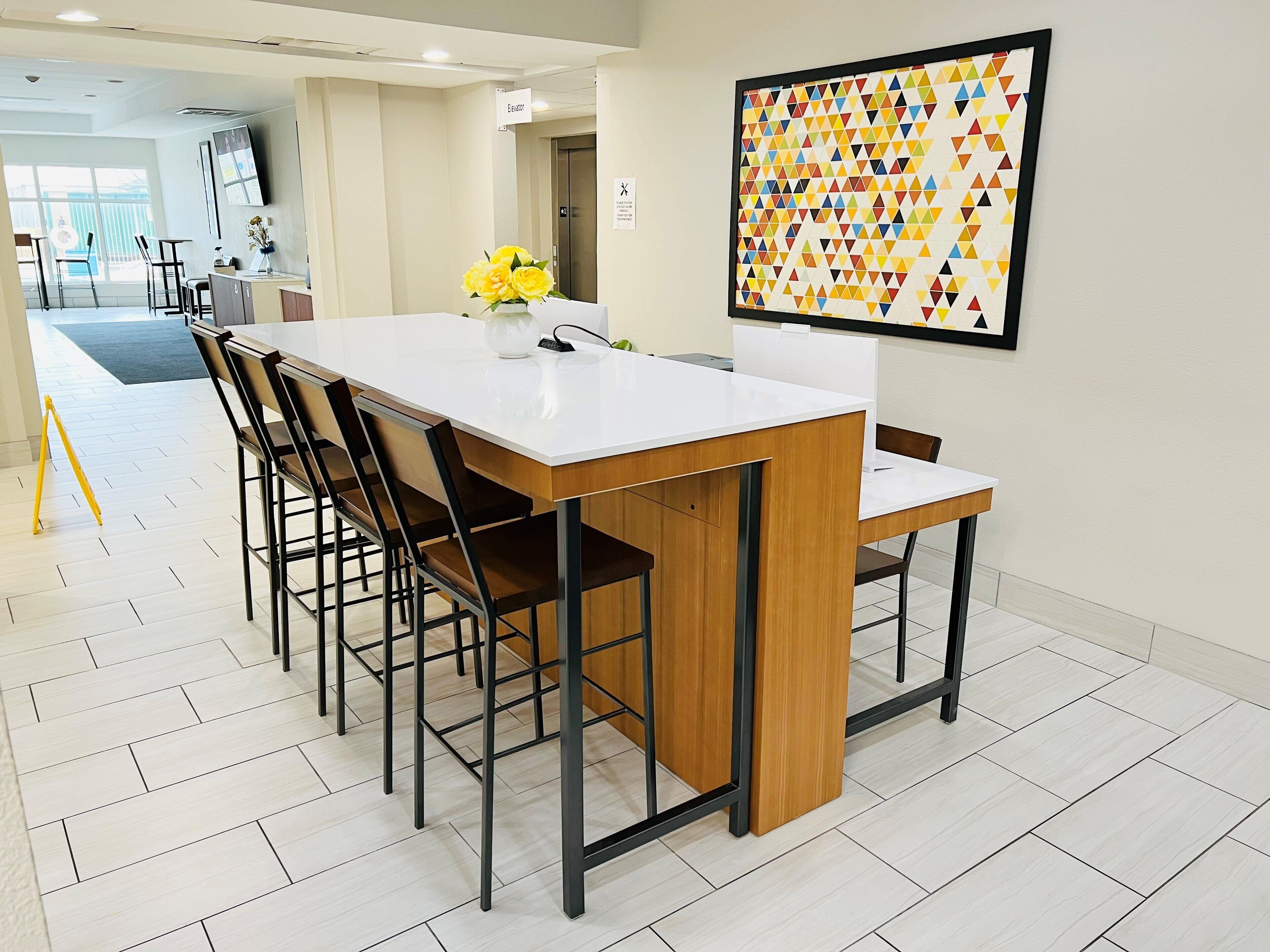 A modern dining area with a white table, wooden chairs, and a colorful geometric artwork on the wall.