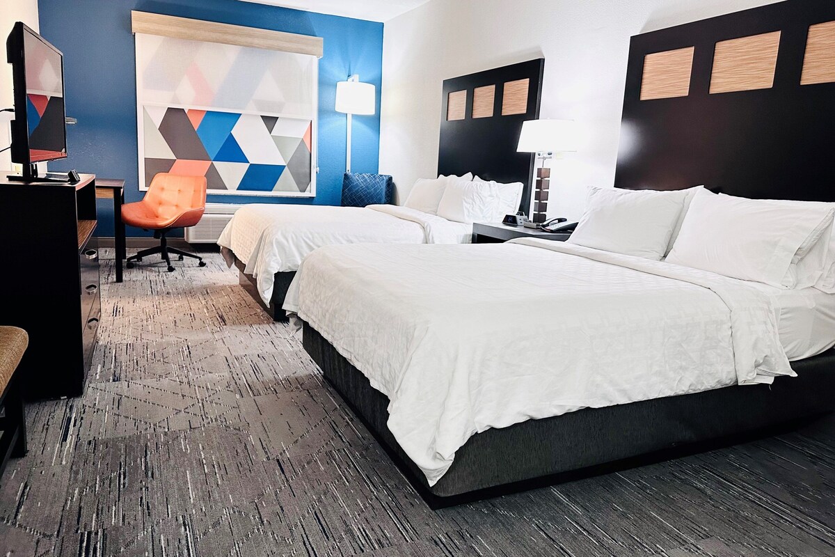 A hotel room with two beds, a desk with a computer, a chair, and a decorative wall with geometric patterns.