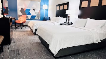 A hotel room with a large bed, a desk with a chair, a TV, and a wall with geometric patterns.