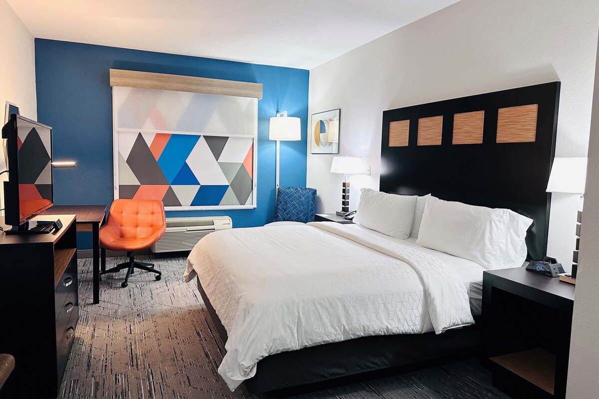 A hotel room with a bed, desk, chair, and a geometric-patterned wall.