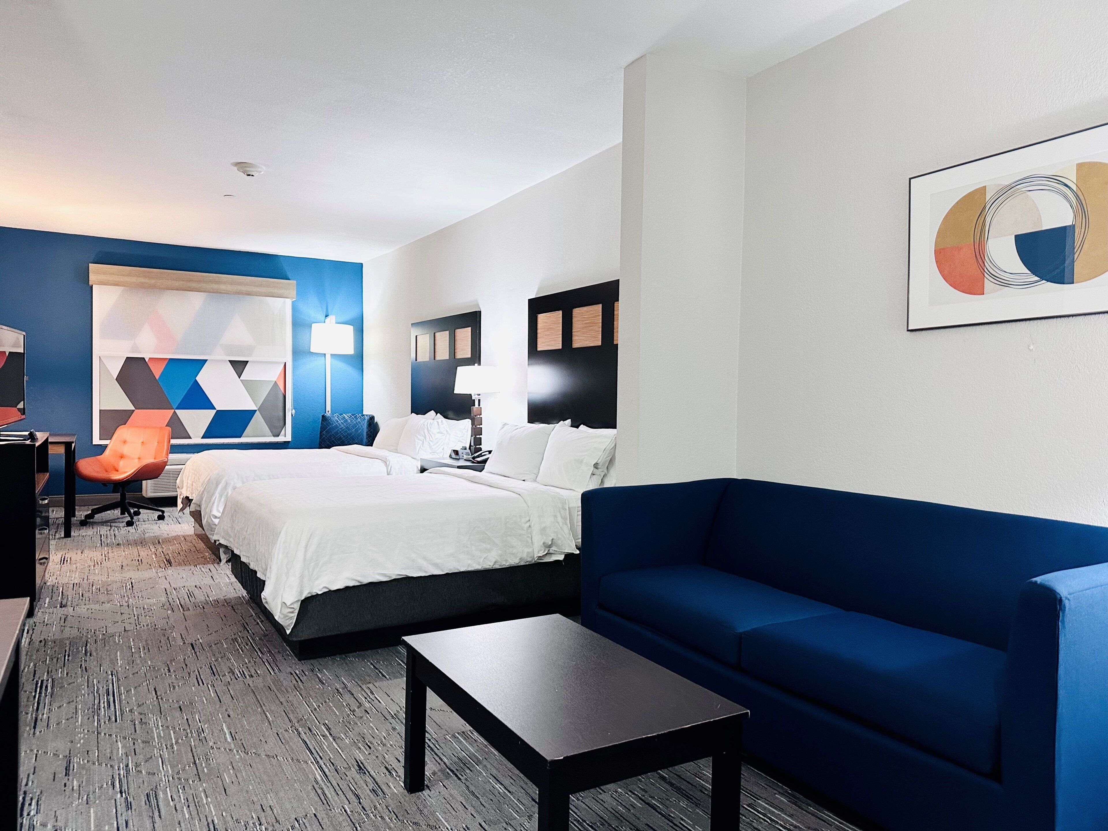 A hotel room with a bed, a blue sofa, a desk, and a chair.