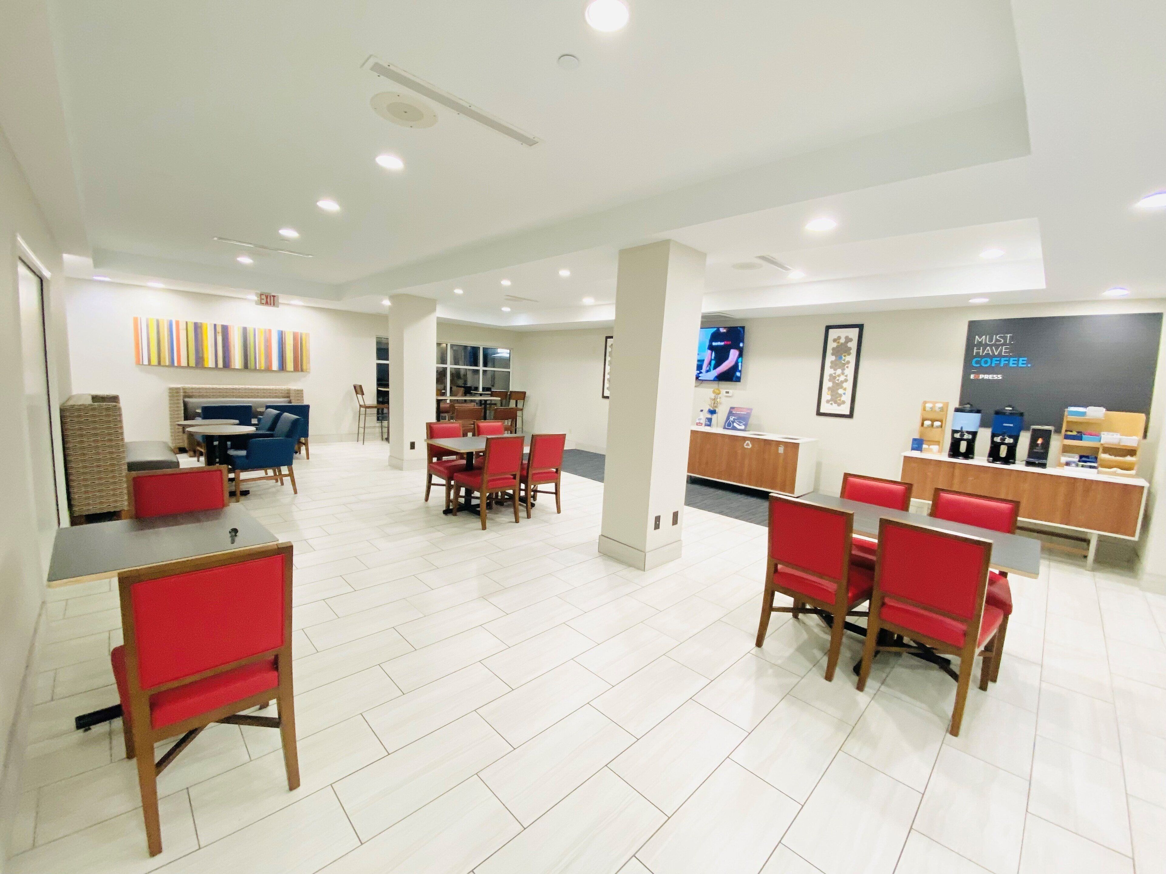 A spacious hotel lobby with a reception desk, seating areas, and a coffee station.