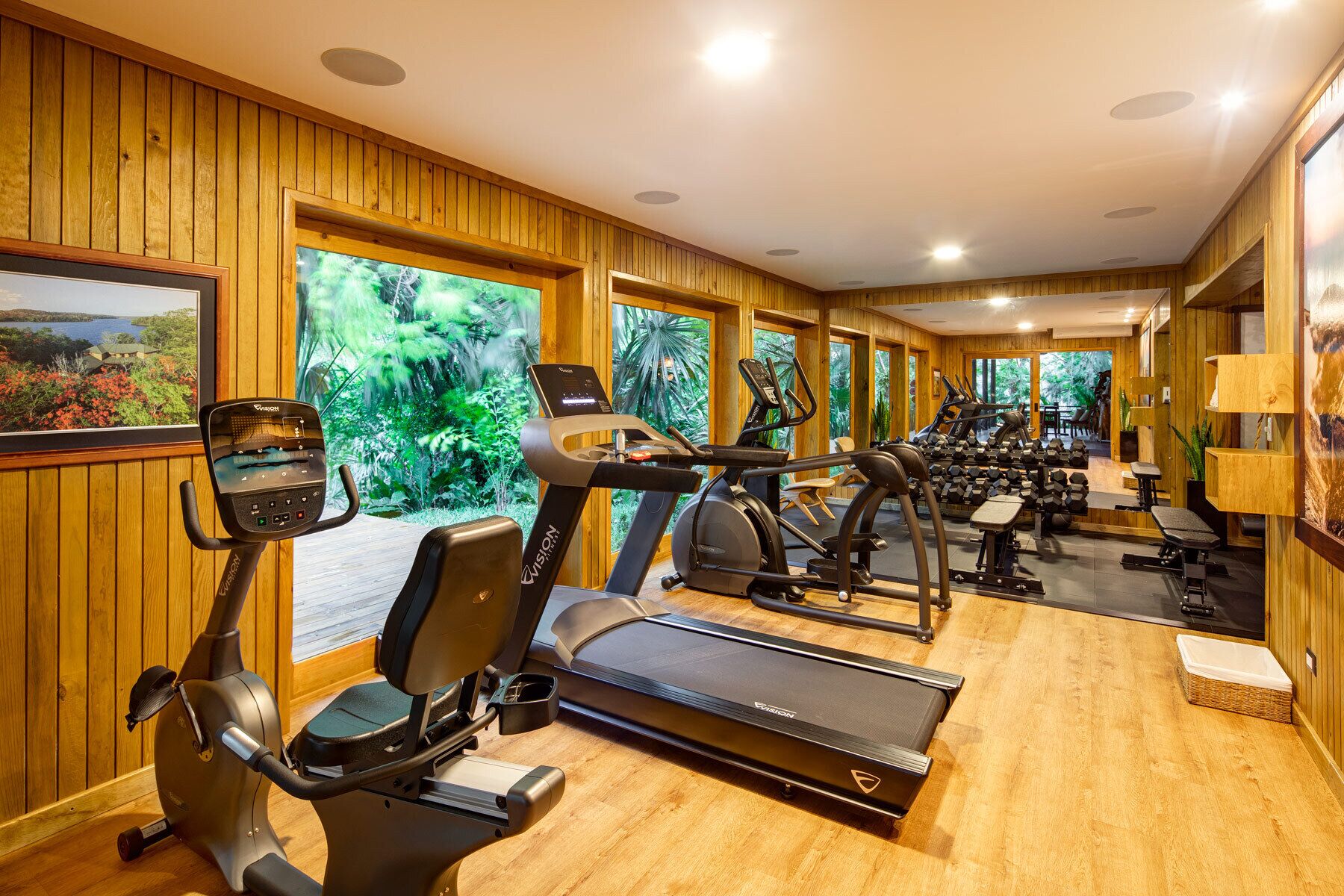 A gym with cardio equipment, wooden walls, and large windows.