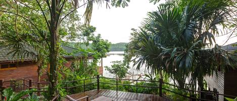 A wooden deck with seating, surrounded by lush greenery and overlooking a body of water.
