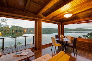 Eine Holzterrasse mit Esstisch und Stühlen, mit Blick auf einen stillen See und bewaldete Hügel.
