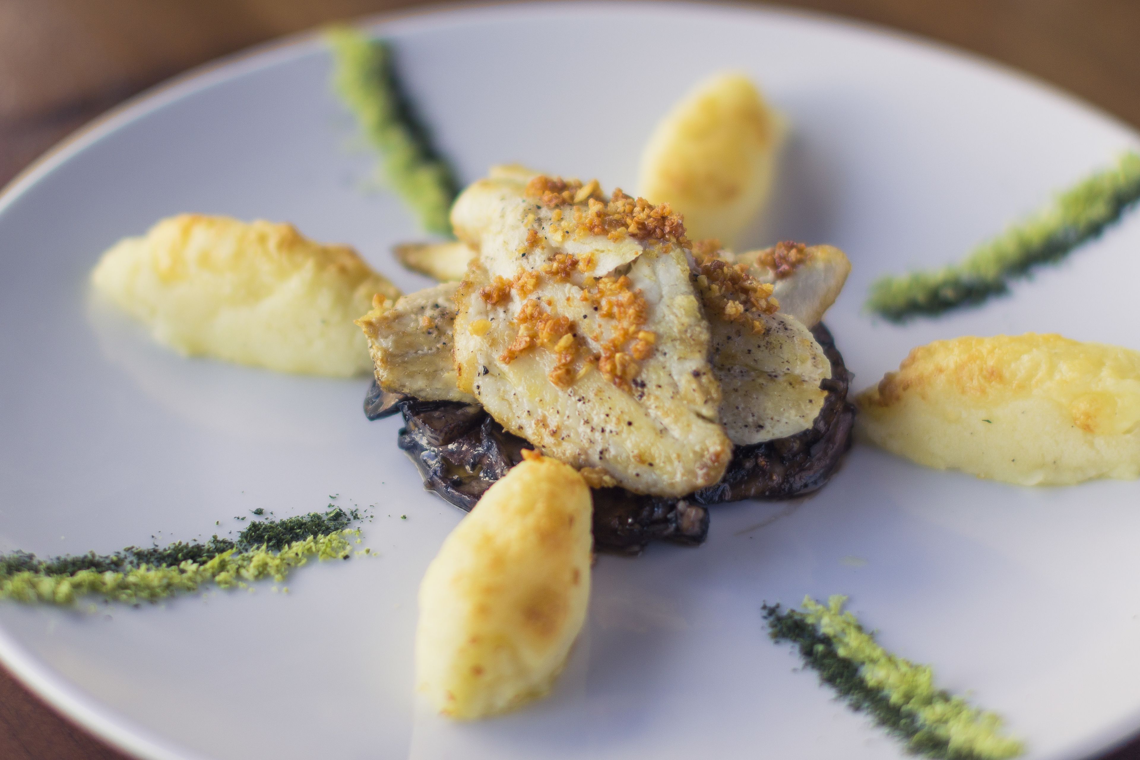 A plate of food with a fish fillet, potatoes, and a garnish.
