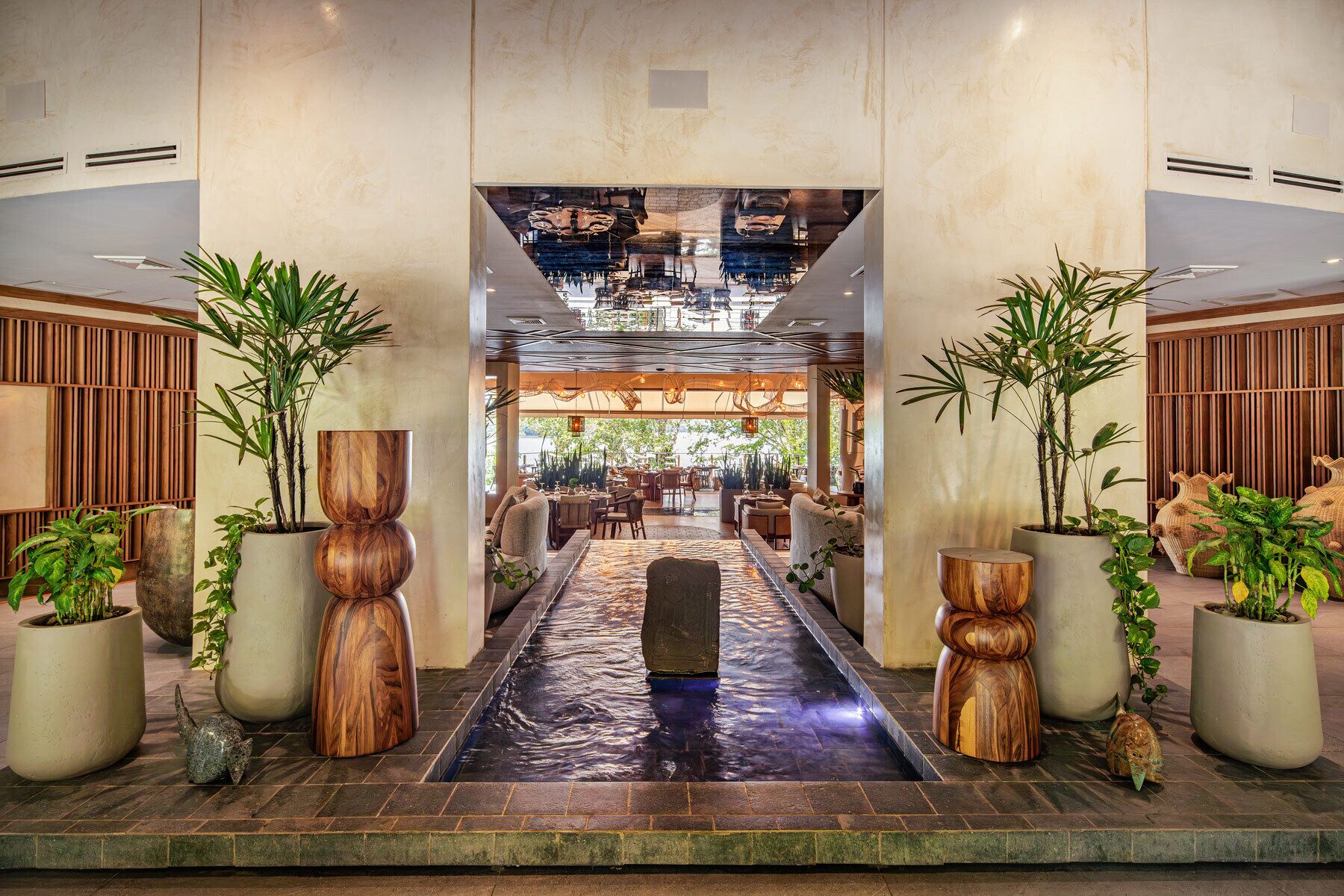 A hotel lobby with a central water feature, seating areas, and potted plants.