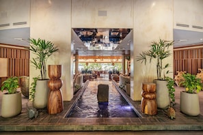 Un hall d’hôtel doté d’un élément décoratif central en eau, d’espaces aménagés pour s’asseoir et de plantes en pot.