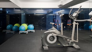 Un gimnasio con una máquina elíptica, pelotas de ejercicio y mancuernas.