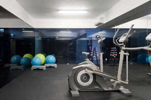 Une salle de sport équipée d’un appareil elliptique, de ballons d’exercice et d’haltères.