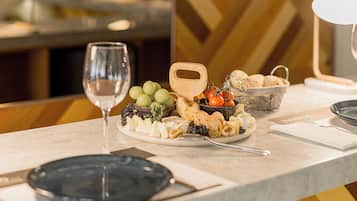 Zona de bar con un esbelón para copas de vino, una selección de quesos, frutas y pan sobre una encimera de mármol.