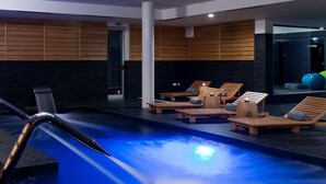 Un área de piscina interior moderna con tragaluces, tumbonas de madera y techo transparente.