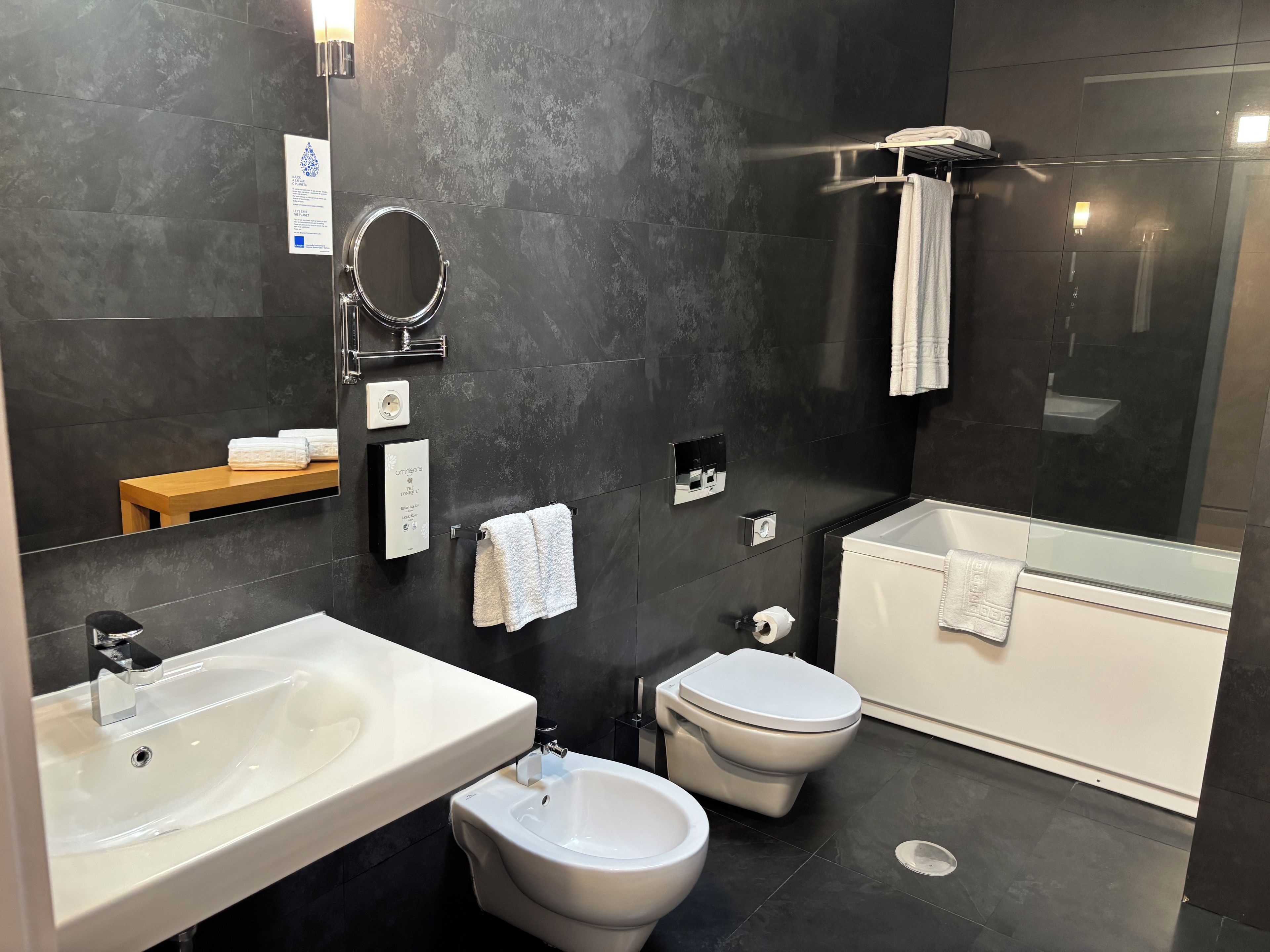 A modern bathroom with a large mirror, a sink, a bidet, a toilet, and a bathtub.
