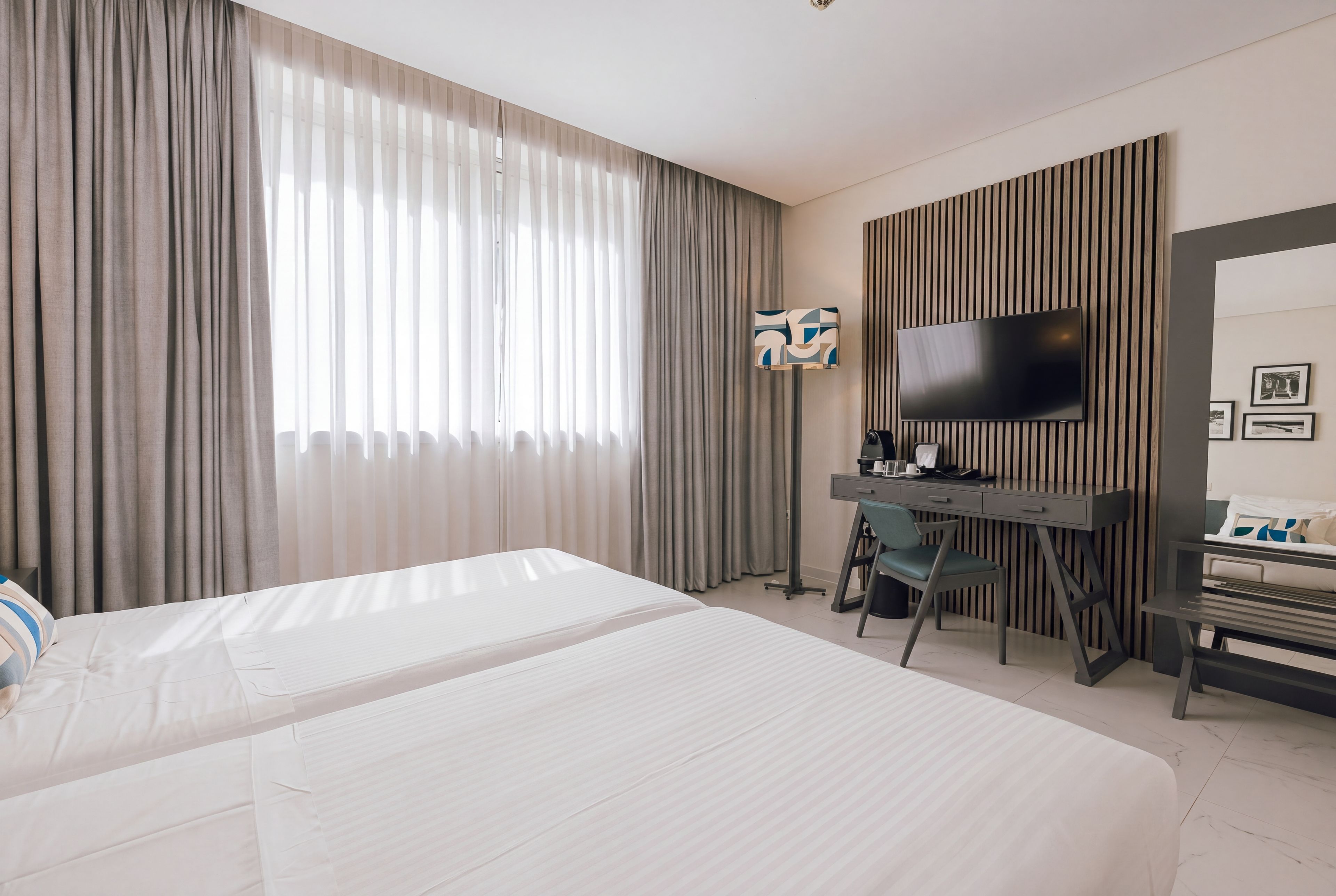 Habitación de hotel con una cama grande, un escritorio con ordenador, un televisor y una ventana con cortinas.