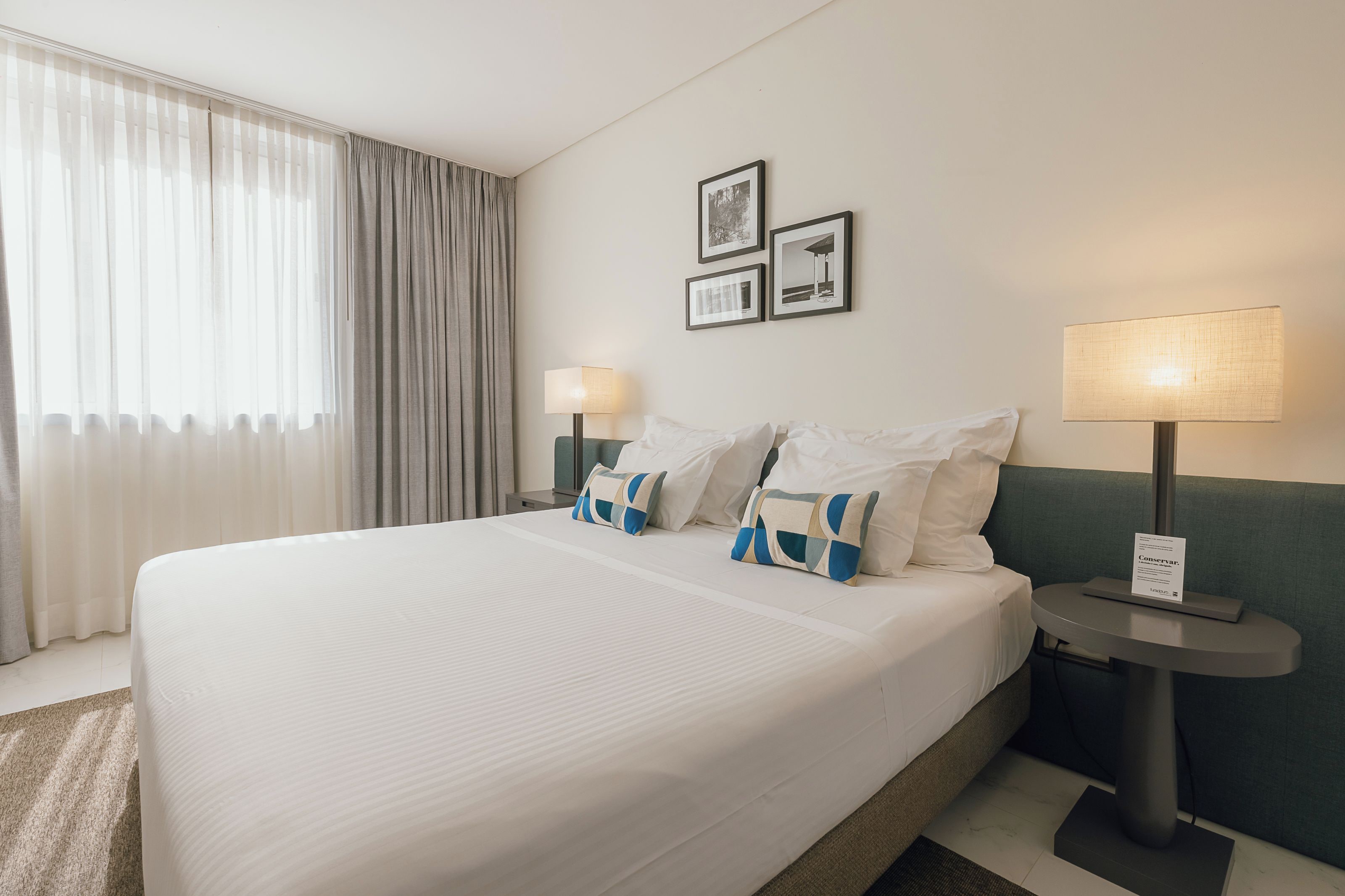 A hotel room with a large bed, two bedside tables, a lamp, and a window with curtains.