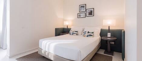 A modern hotel room with a large bed, two bedside tables, a nightstand, and a wall-mounted lamp.