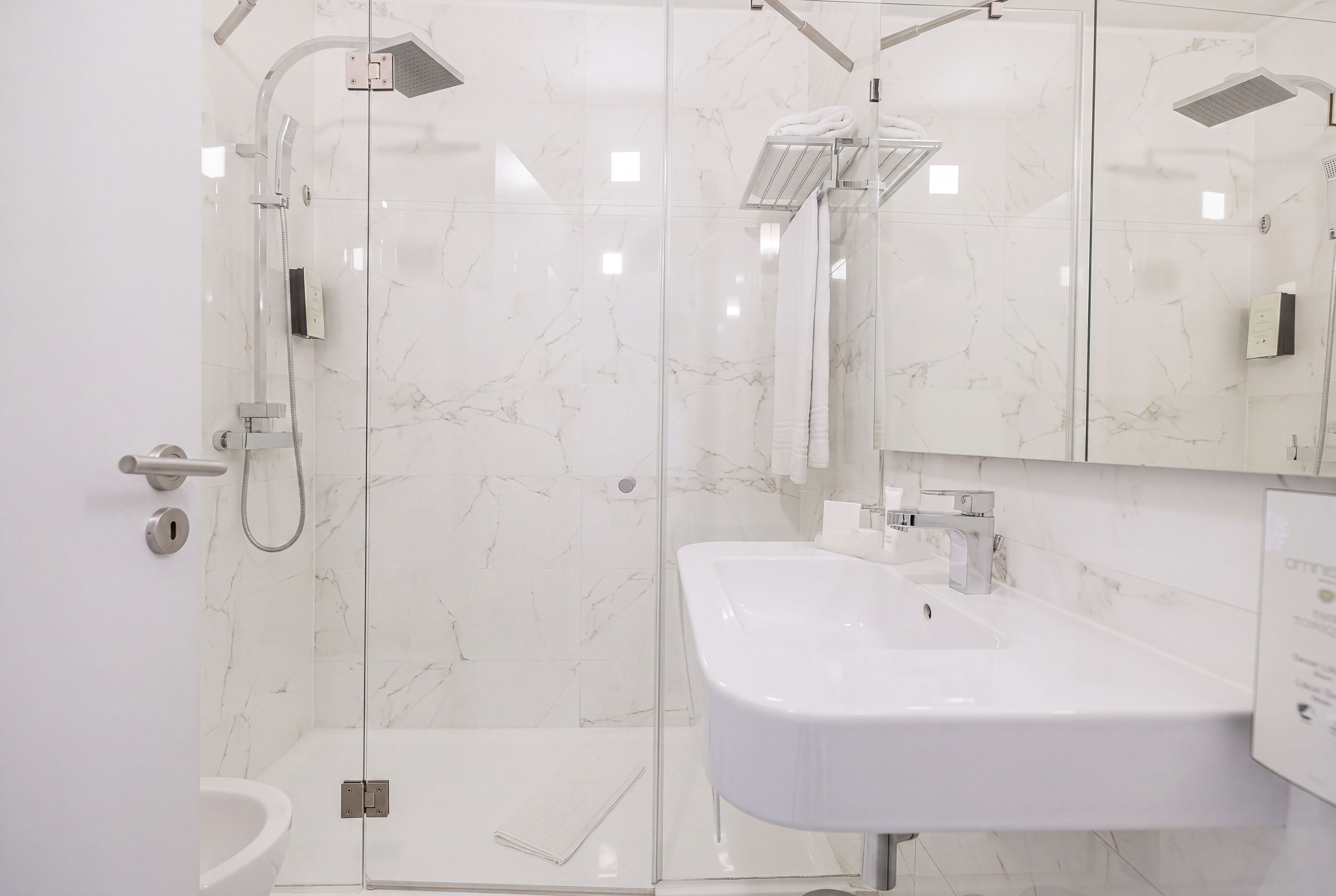 Un baño moderno con cabina de ducha de vidrio, un lavamanos blanco y pared con azulejos de mármol.