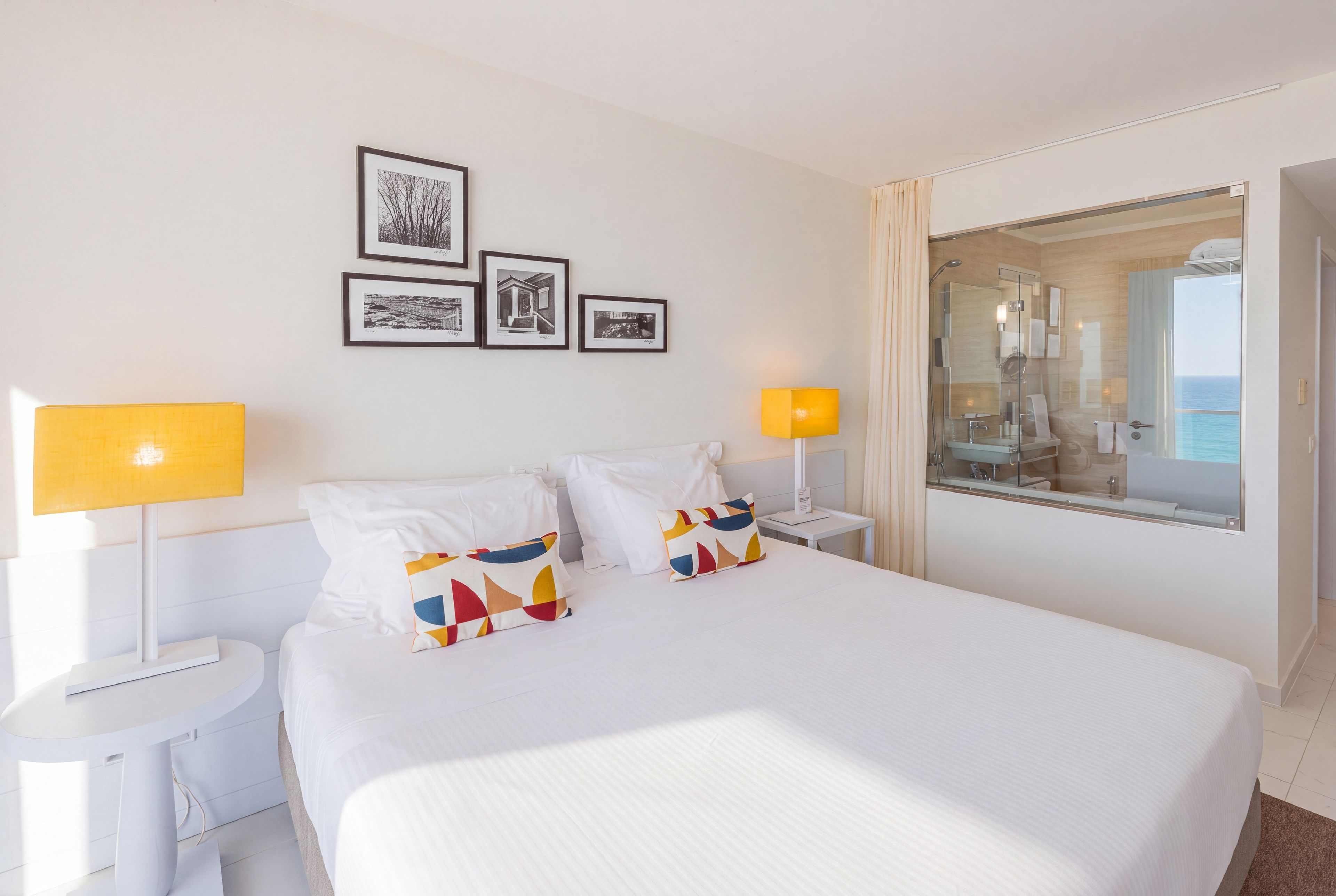 A hotel room with a bed, two bedside lamps, a nightstand, a mirror, and framed pictures on the wall.