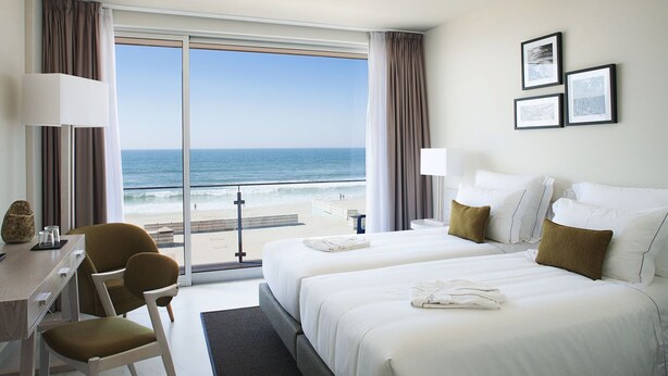 Habitación de hotel con dos camas, un escritorio, una silla y vista a la playa.