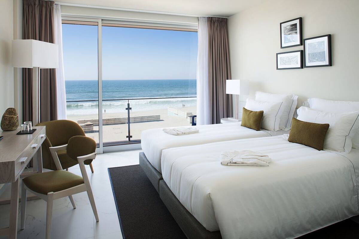 Habitación de hotel con dos camas, un escritorio, una silla y vista a la playa.