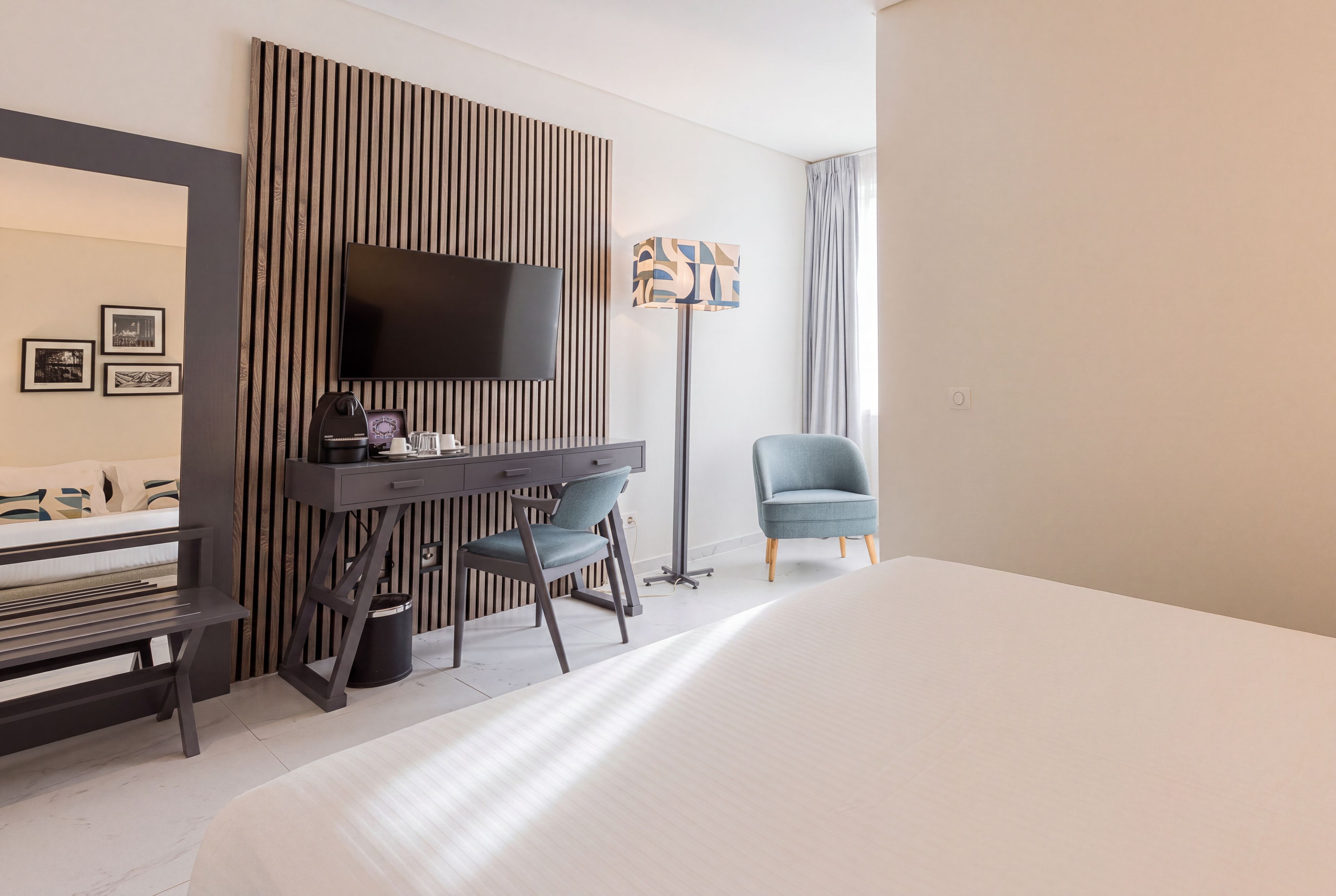 Habitación de hotel con cama, escritorio, silla, televisor de pantalla plana y lámpara de pie.
