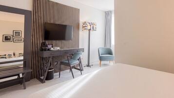 Habitación de hotel con cama, escritorio, silla, televisor de pantalla plana y lámpara de pie.