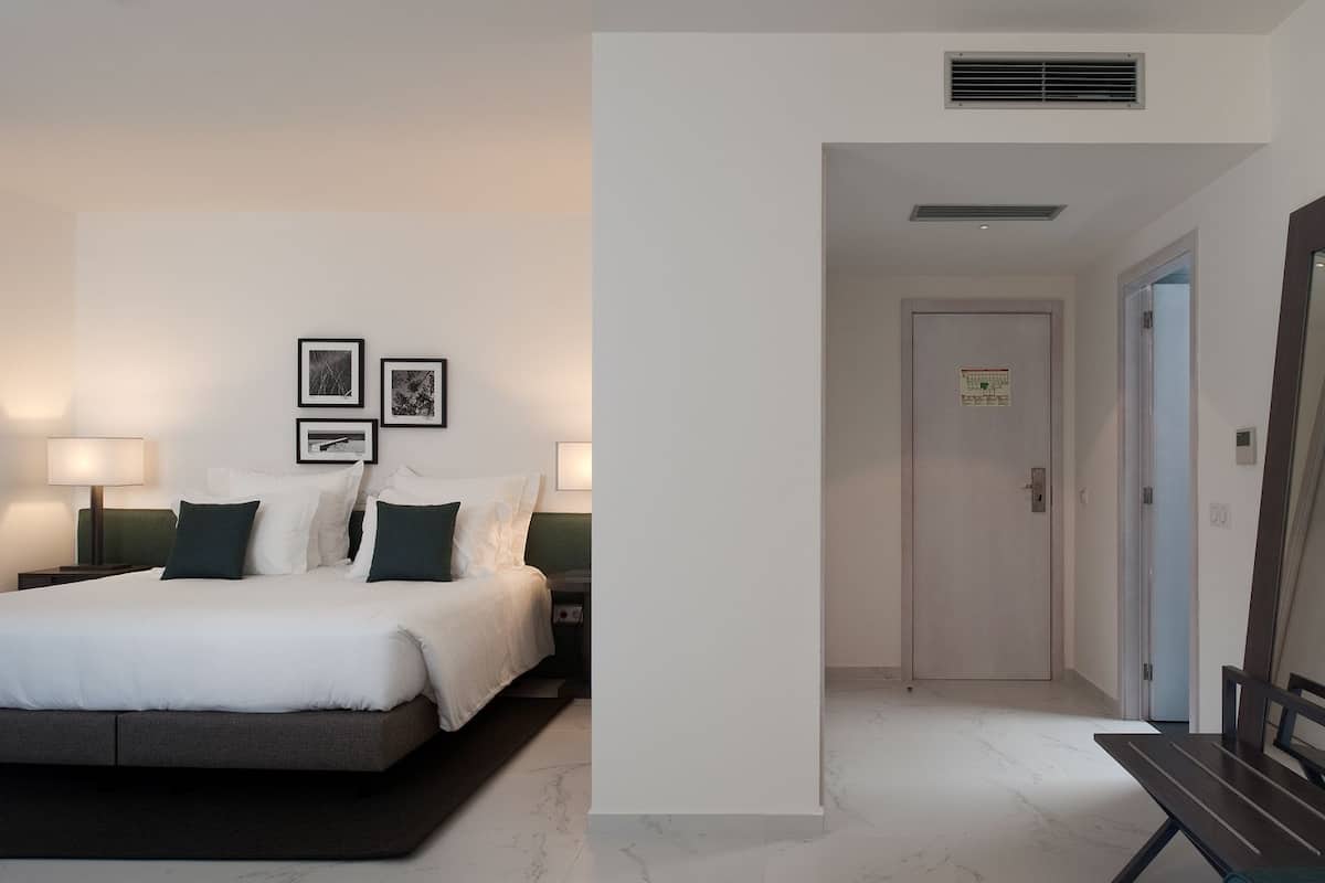Habitación de hotel con cama, lámparas de noche, televisión de pantalla plana y puerta que da a otra habitación.