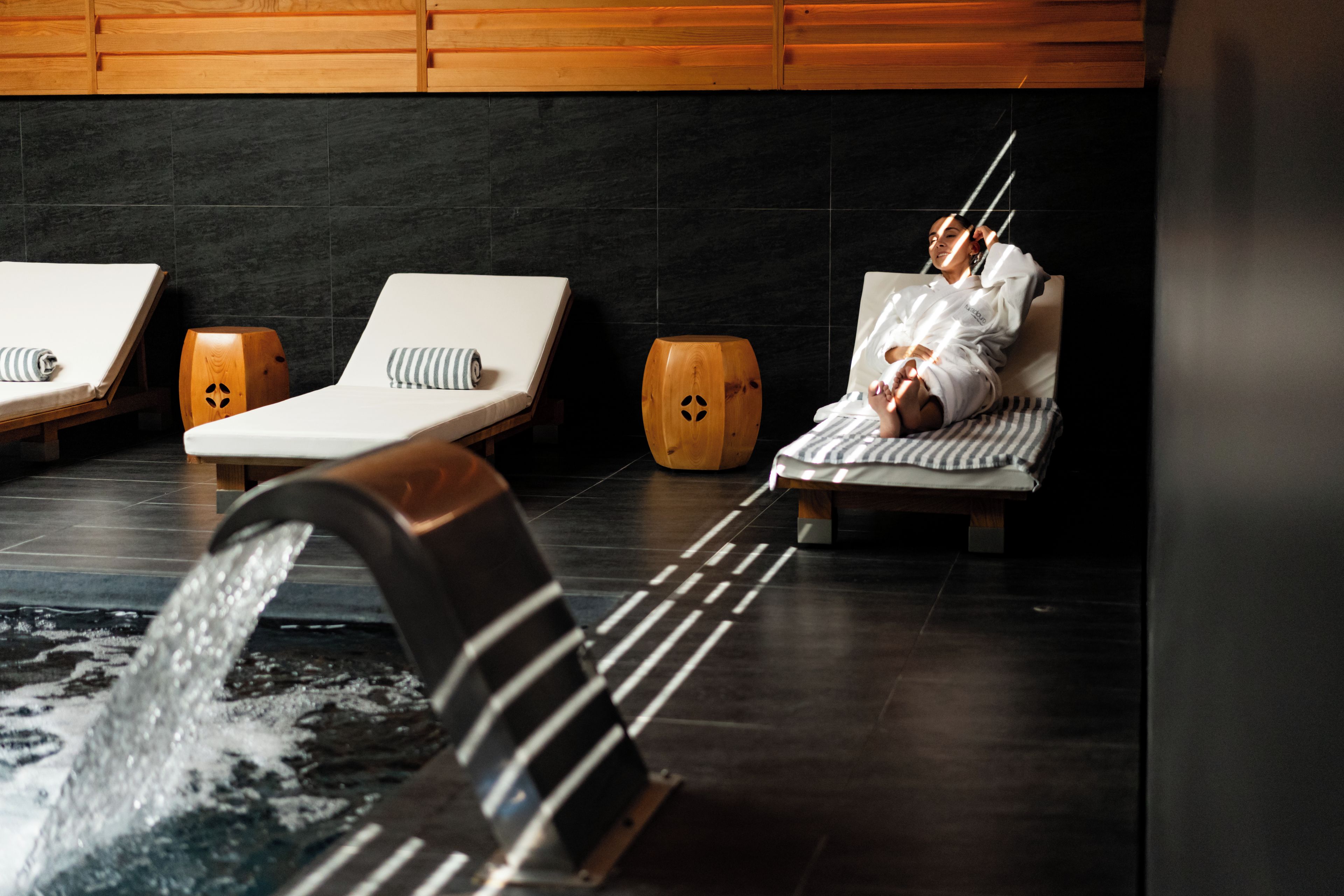 A spa area with three lounge chairs, a wooden bench, and a water feature.