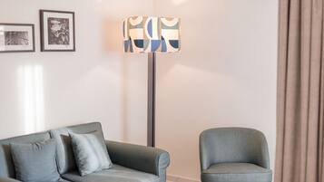 Una sala de estar moderna con un sofá gris, un sillón a juego, una lámpara de pie con pantalla geométrica y dos cuadros en la pared.