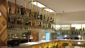 Eine Bar mit Regalen voller Spirituosenflaschen und Gläsern, einer Theke mit einem Computer und leuchtend grünen Stühlen.