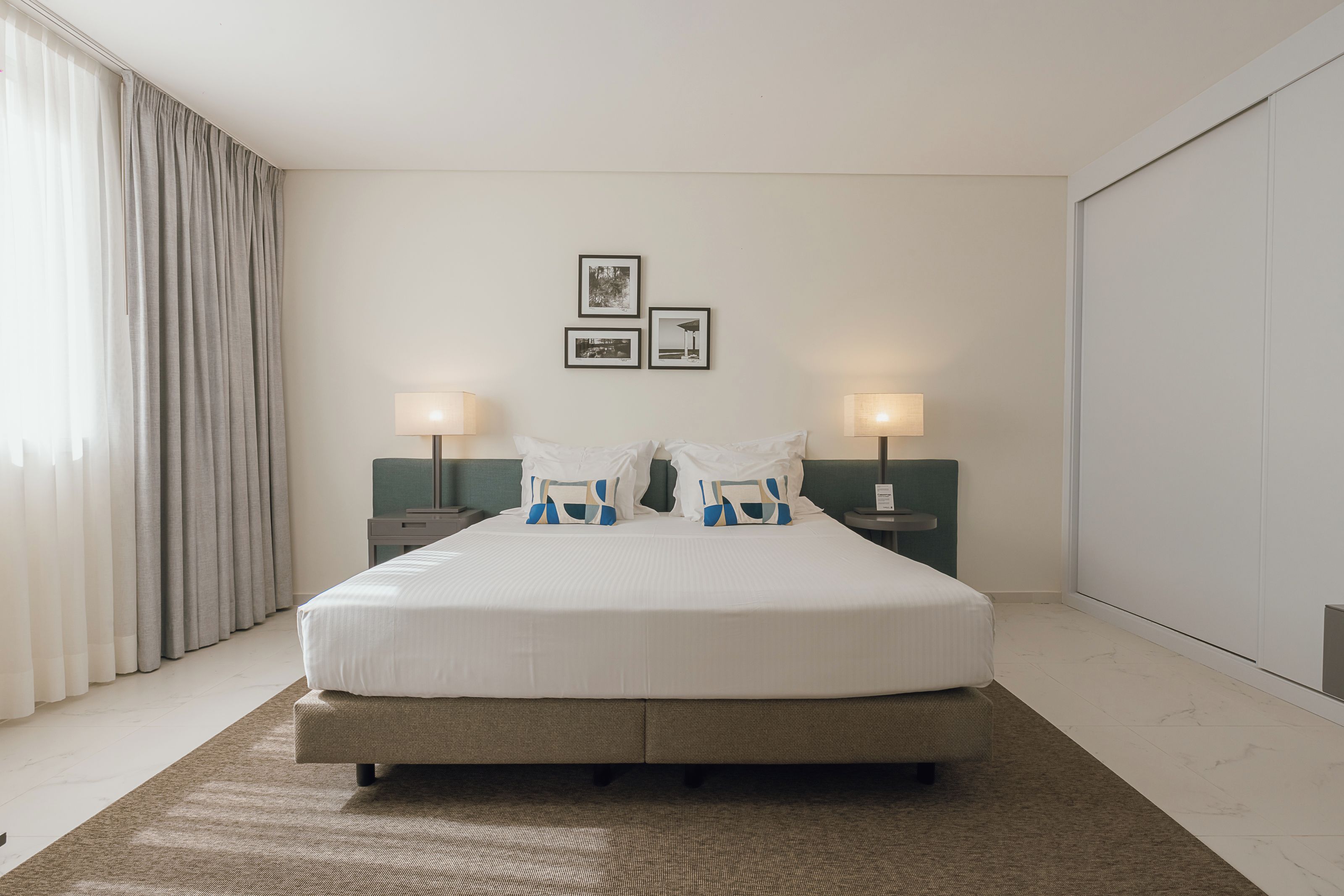 A hotel room with a large bed, two bedside tables with lamps, a headboard, and a view of the outside.