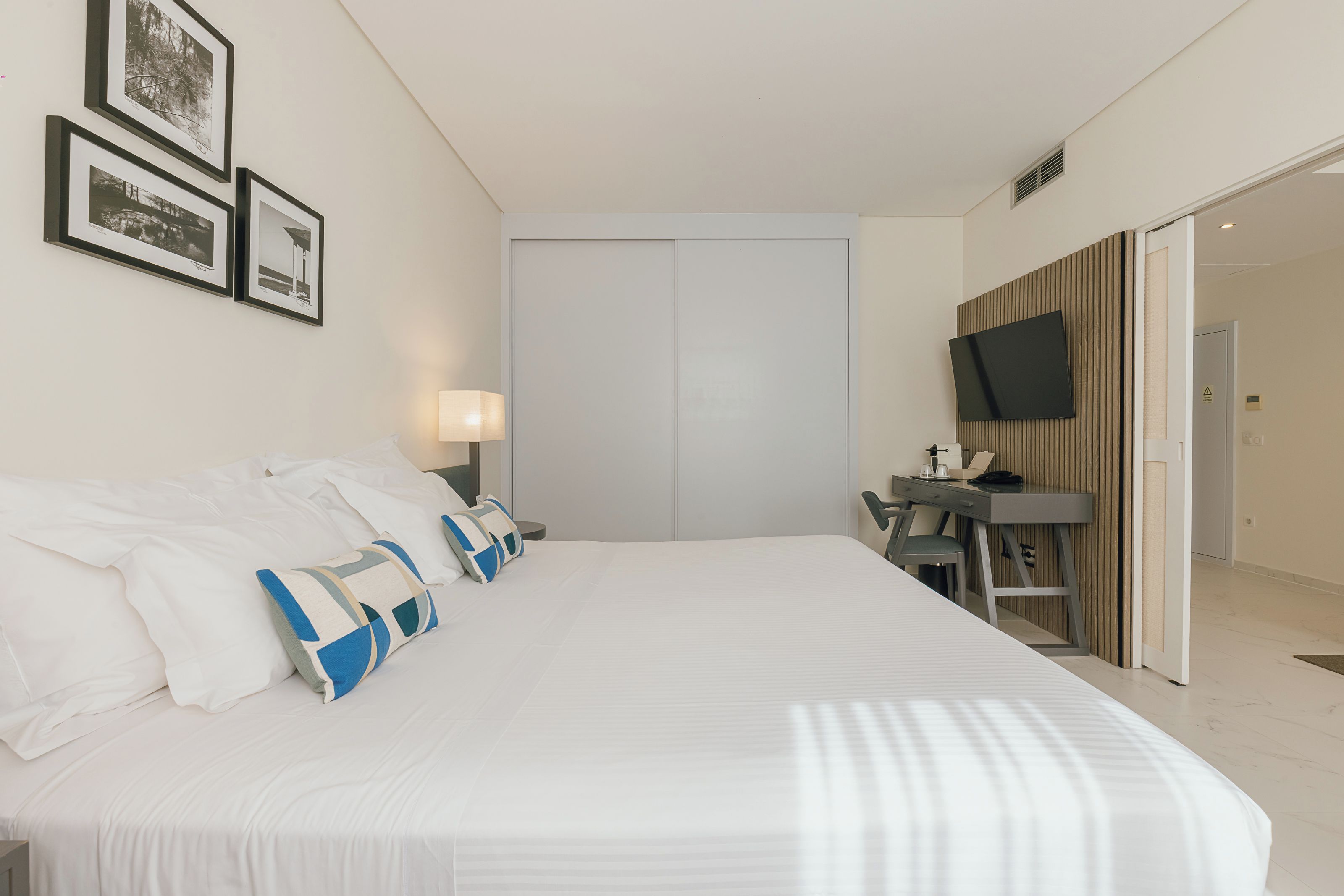 A hotel room with a large bed, a desk, a television, and a wardrobe.